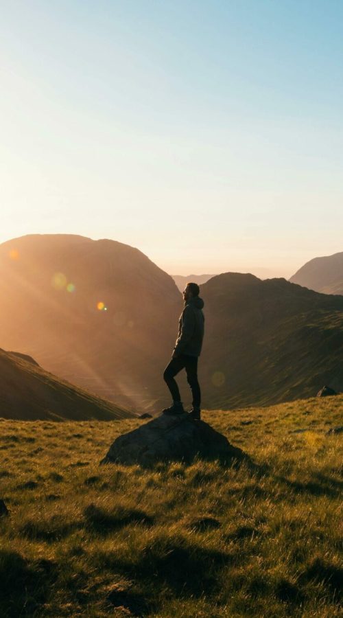 Silhouette of a person standing on a hill during sunrise in Cumbria, England with scenic mountain views.