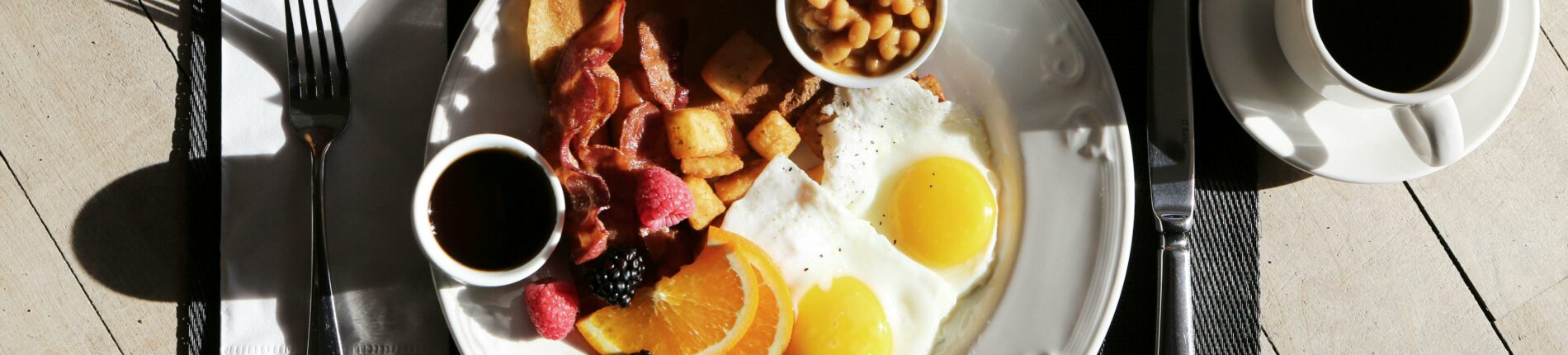 A delicious breakfast spread featuring eggs, bacon, fruit, and coffee on a sunlit table.