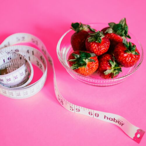 A glass bowl of fresh strawberries paired with a pink measuring tape symbolizes healthy eating.