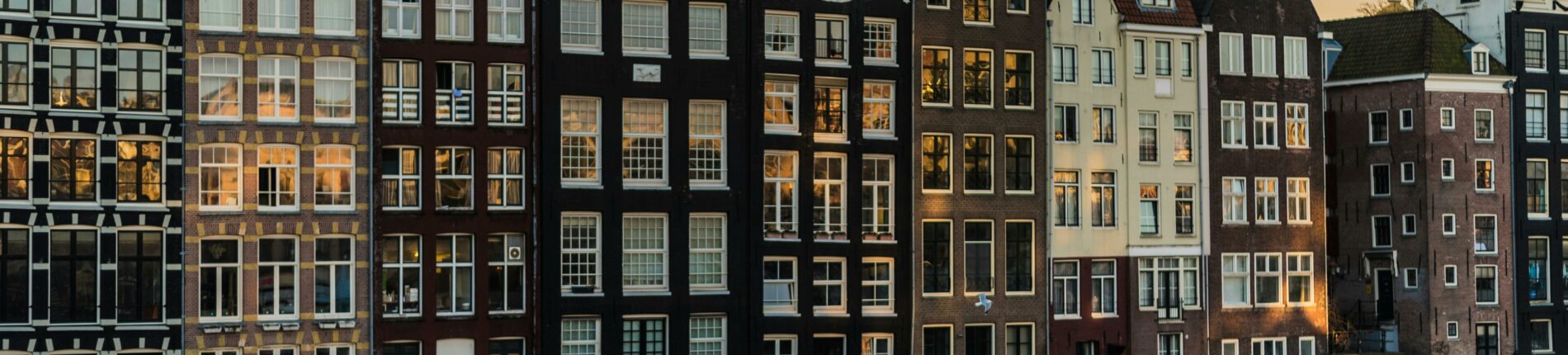 Scenic view of iconic canal houses in Amsterdam with reflections in the water during sunset.