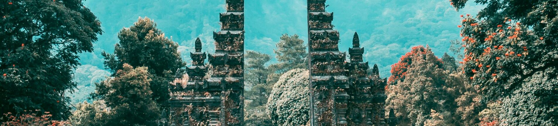 Majestic Balinese gate amidst a lush, tropical landscape and towering mountains, under a bright sky.