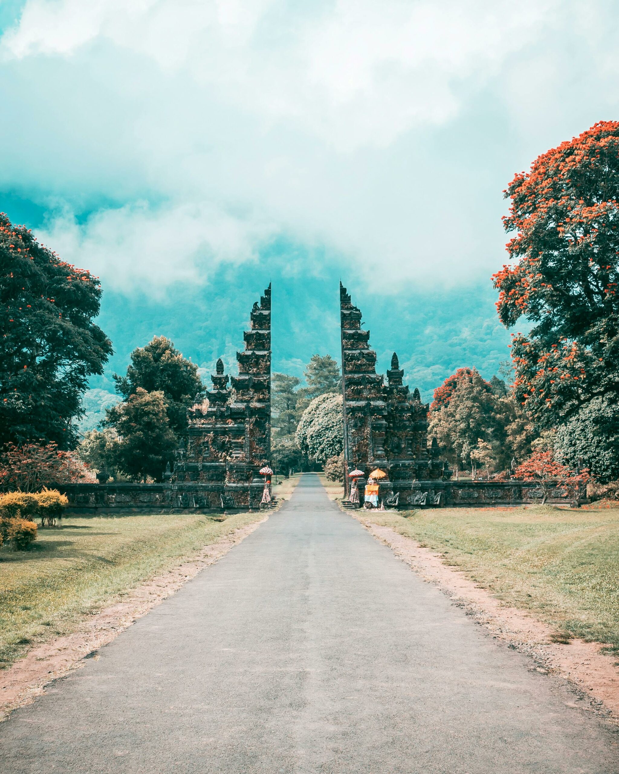 Majestic Balinese gate amidst a lush, tropical landscape and towering mountains, under a bright sky.