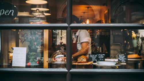Warm bakery scene in London through window showcasing pastries and chef at work.