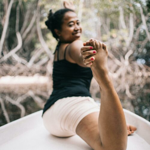 A woman exercises outdoors on a boat, showcasing flexibility in a peaceful natural setting.