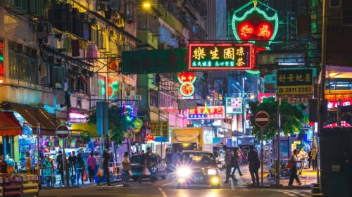 Colorful neon lights illuminate a bustling street in the New Territories, Hong Kong, by night.
