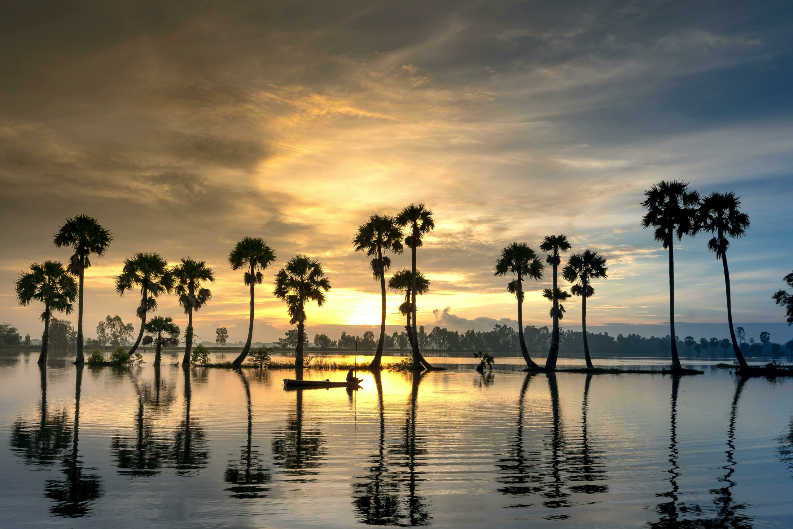A stunning sunset over a tropical lake in Vietnam with palm tree silhouettes and water reflections.