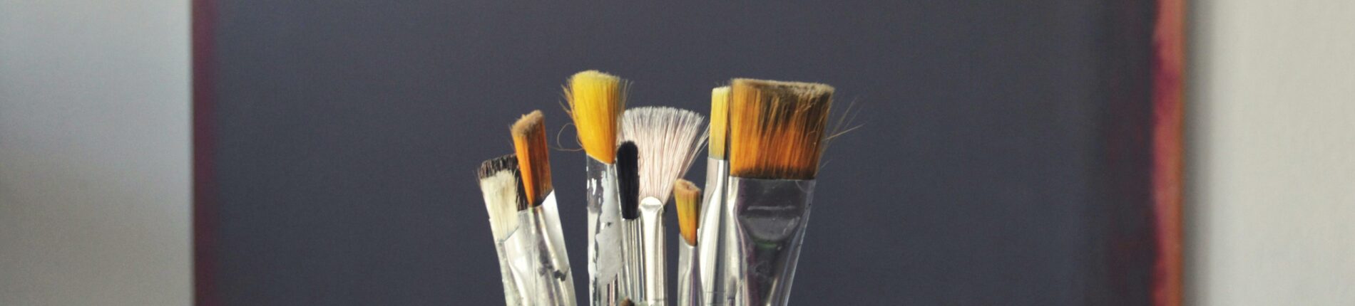 A set of paintbrushes in front of an abstract canvas, reflecting creativity and inspiration.