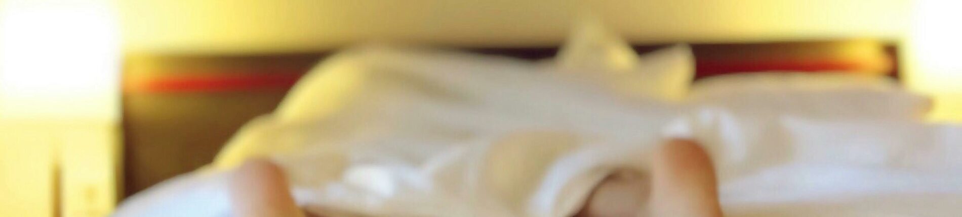 A person relaxing on a bed with feet under white sheets, conveying serenity.