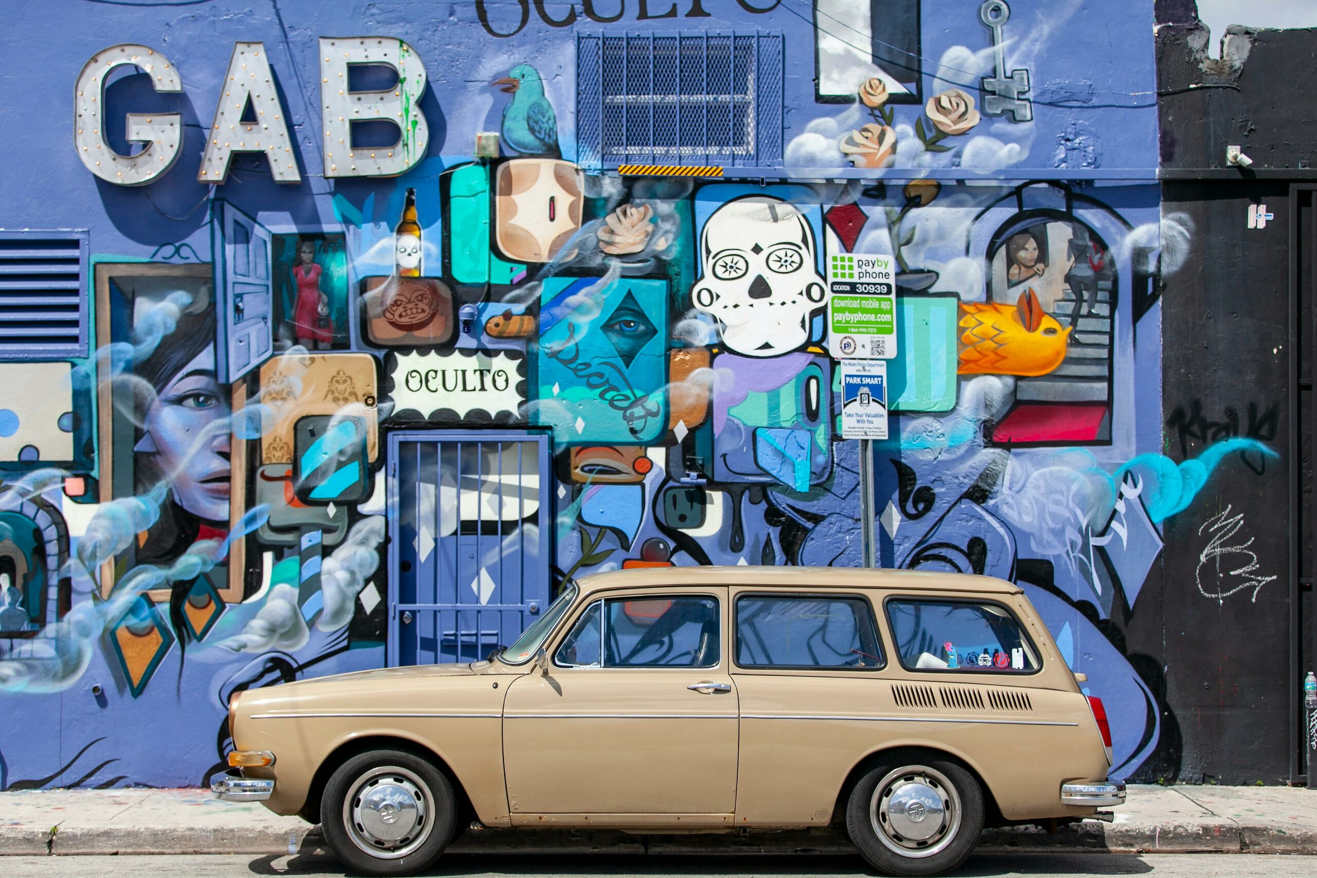A vintage car parked against a vibrant street art mural in Miami, Florida.