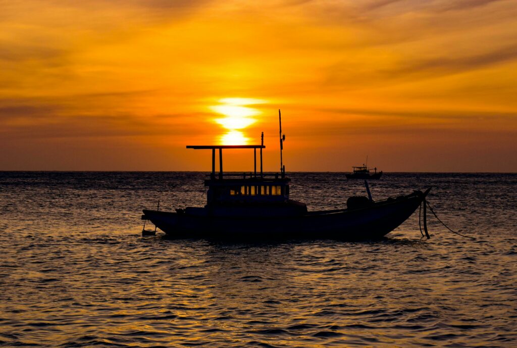 A peaceful fishing boat silhouette against a stunning sunrise over the ocean.