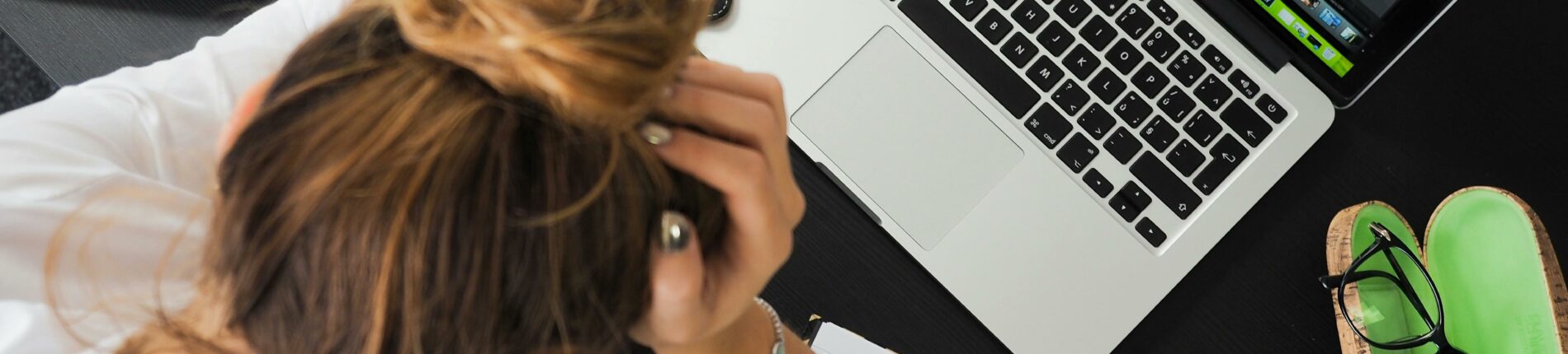 Overhead view of a stressed woman working at a desk with a laptop, phone, and notebooks.