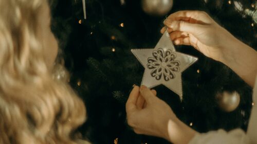A woman places a star ornament on a Christmas tree, symbolizing festive holiday traditions.