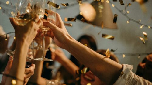 A lively indoor party scene with people toasting champagne glasses amid confetti and warm lights.