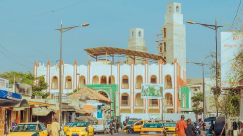 A vibrant street scene featuring an Islamic mosque with distinct architecture under a clear blue sky.