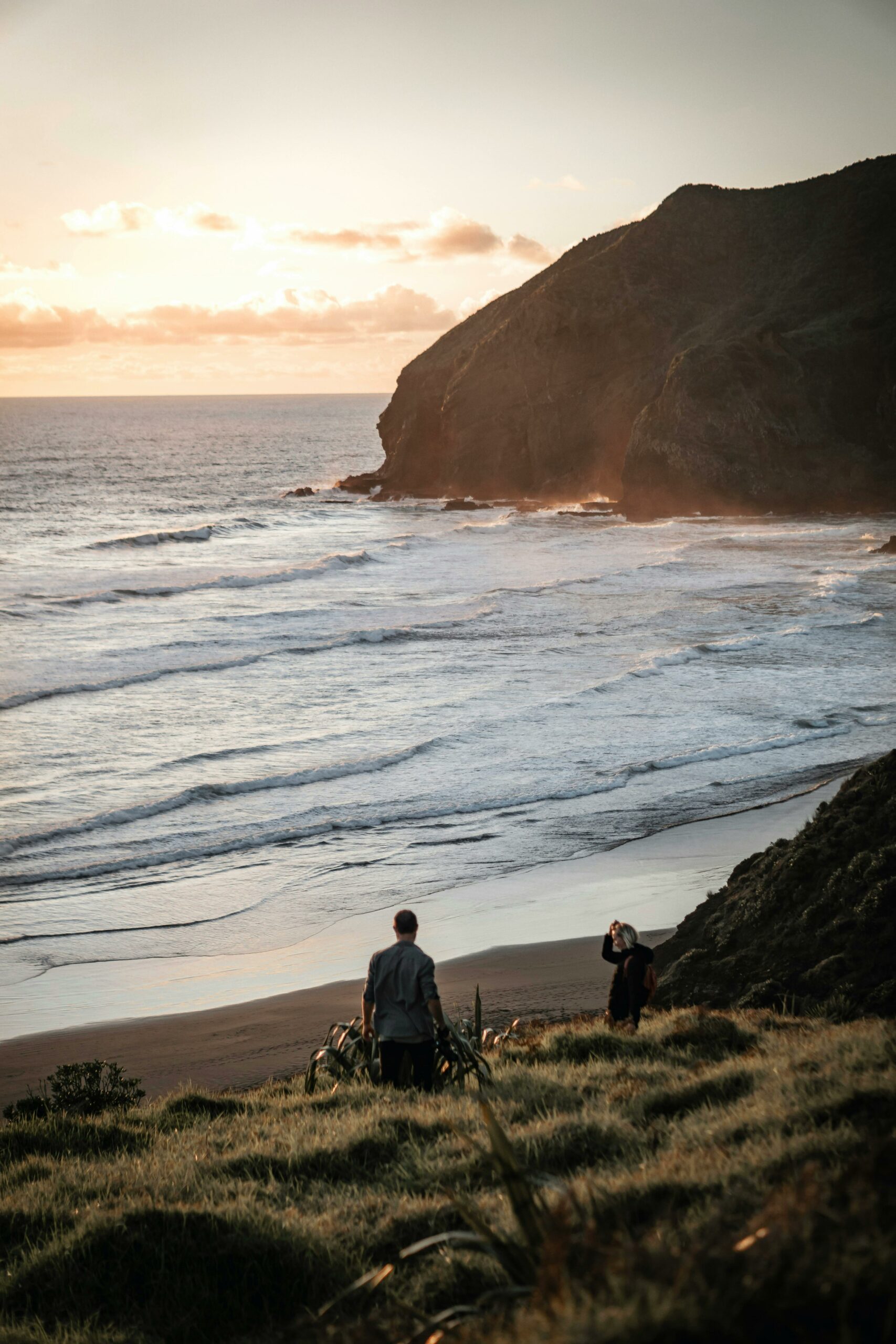 Tranquil New Zealand beach scene at sunset with two people enjoying the view.