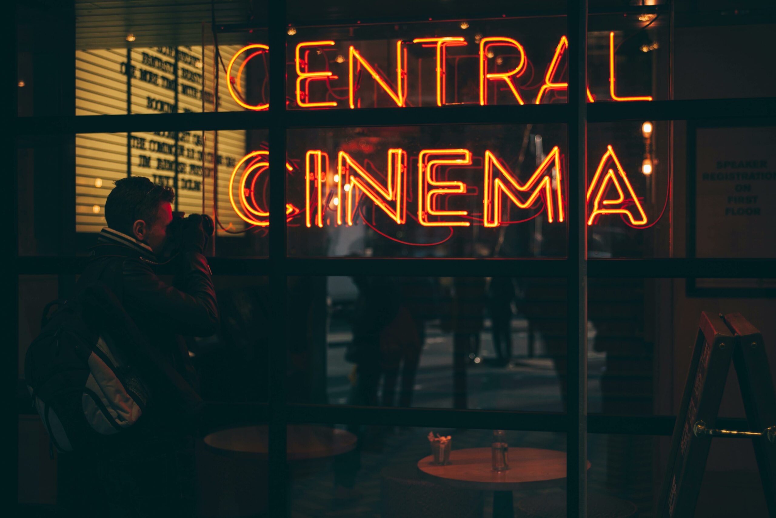 A photographer captures the vibrant neon glow of a cinema sign during the evening.