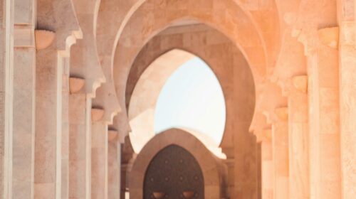 A woman walks through the stunning arches of Hassan II Mosque, Casablanca, highlighting Islamic architecture.
