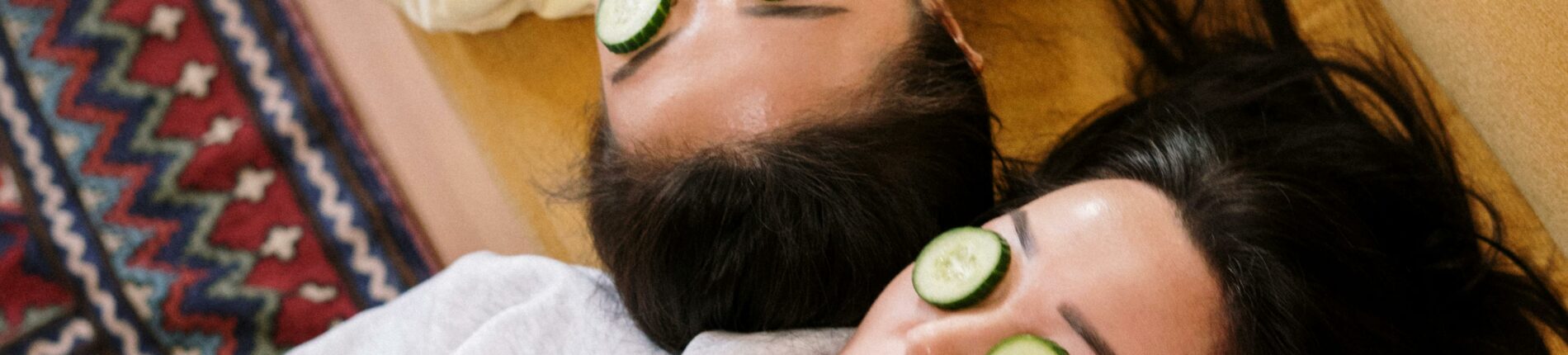 Two women enjoying a relaxing spa day with cucumber masks in a cozy home setting.