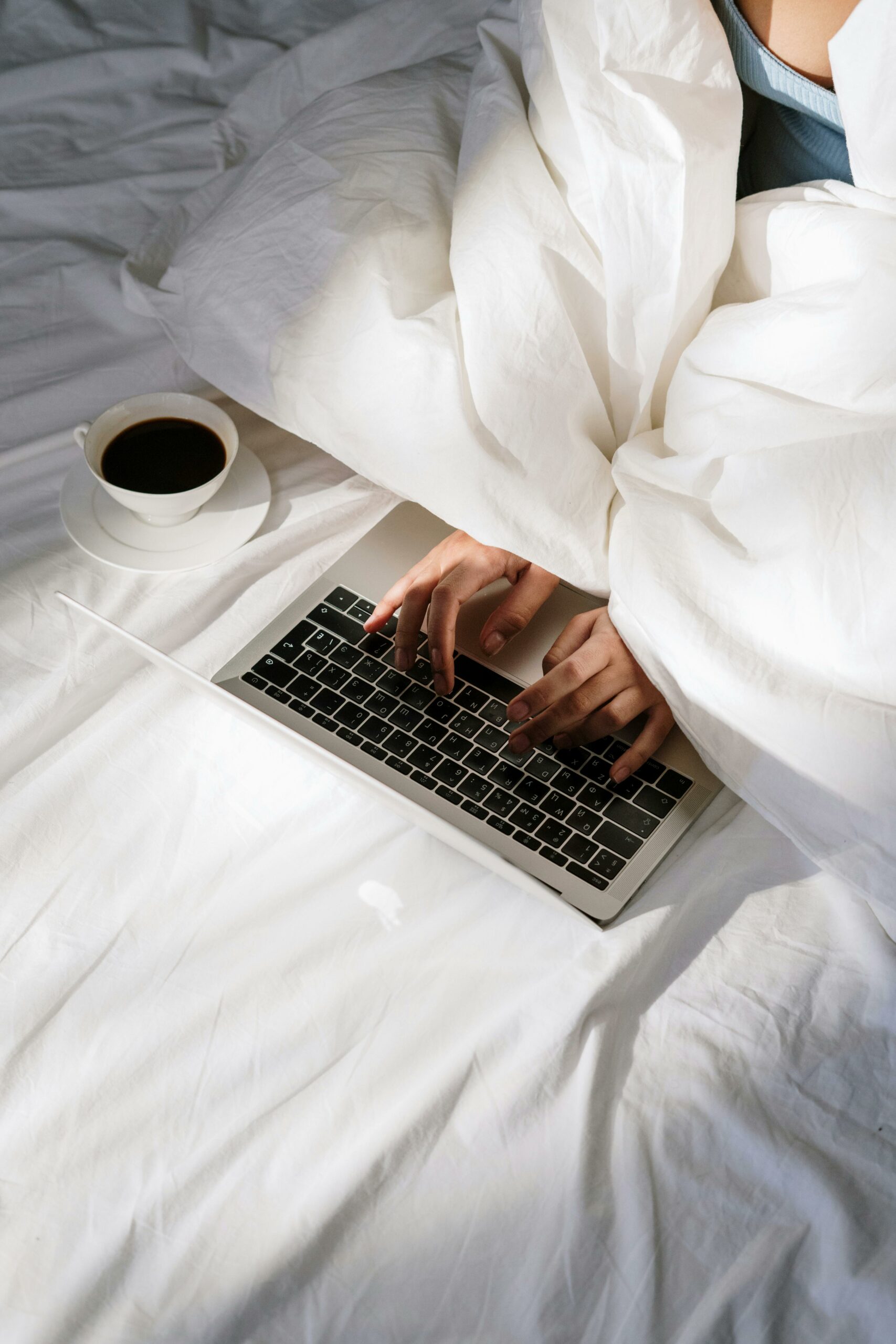 Comfortable home office setup with a laptop on bed and a cup of coffee, perfect for remote work.
