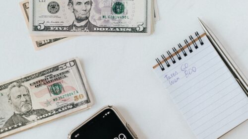 Overhead view of a hand using a calculator with US dollars and notes, representing finance and budgeting.