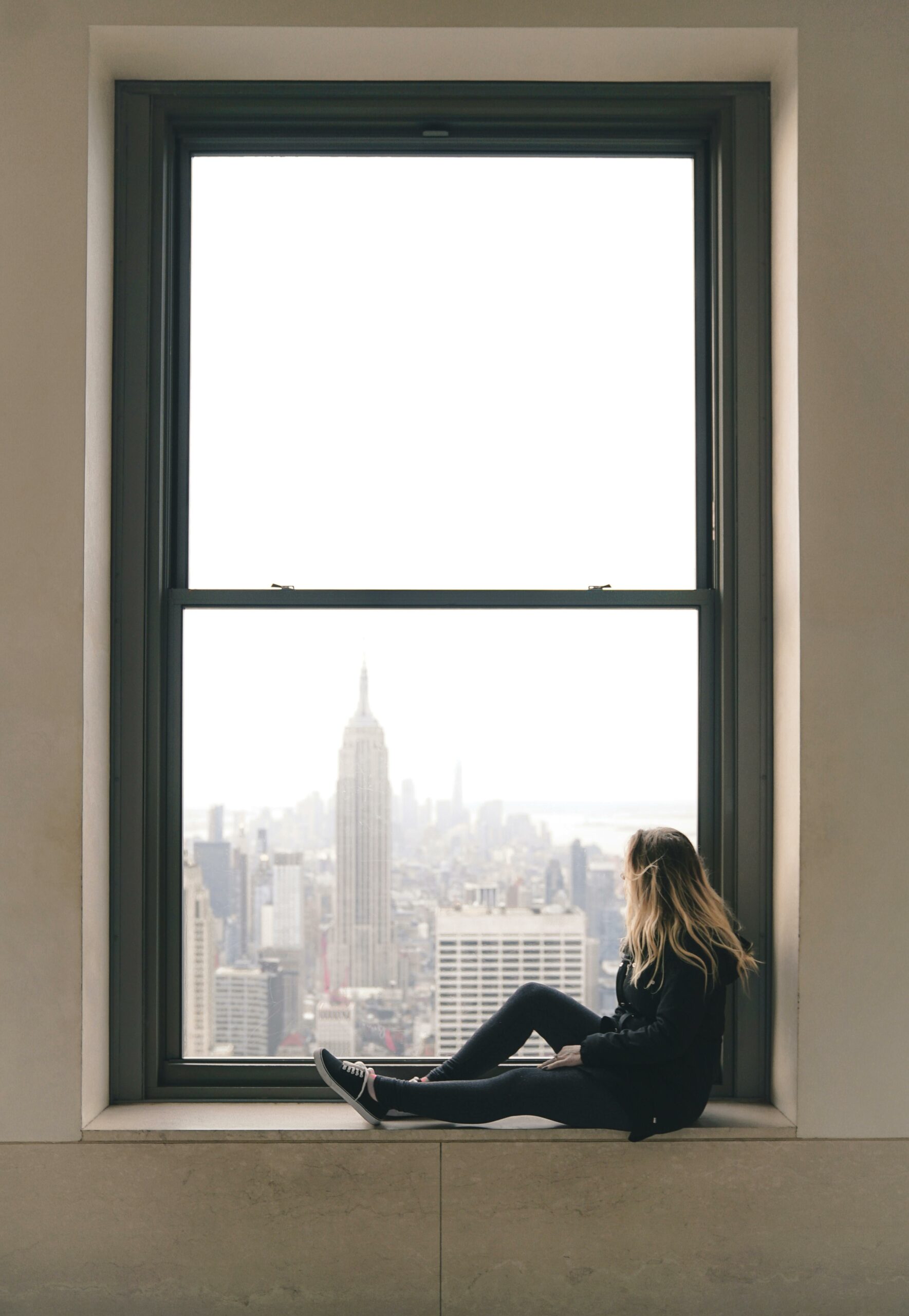 Woman sitting on a window sill with view of the Empire State Building in New York City.