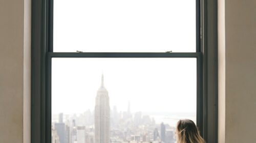 Woman sitting on a window sill with view of the Empire State Building in New York City.