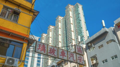 Low angle view of vibrant high-rise buildings in downtown Hong Kong under a clear blue sky.