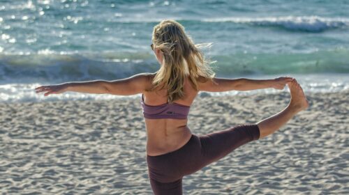 A woman performs yoga on a sandy beach at sunrise, embracing wellness and tranquility.