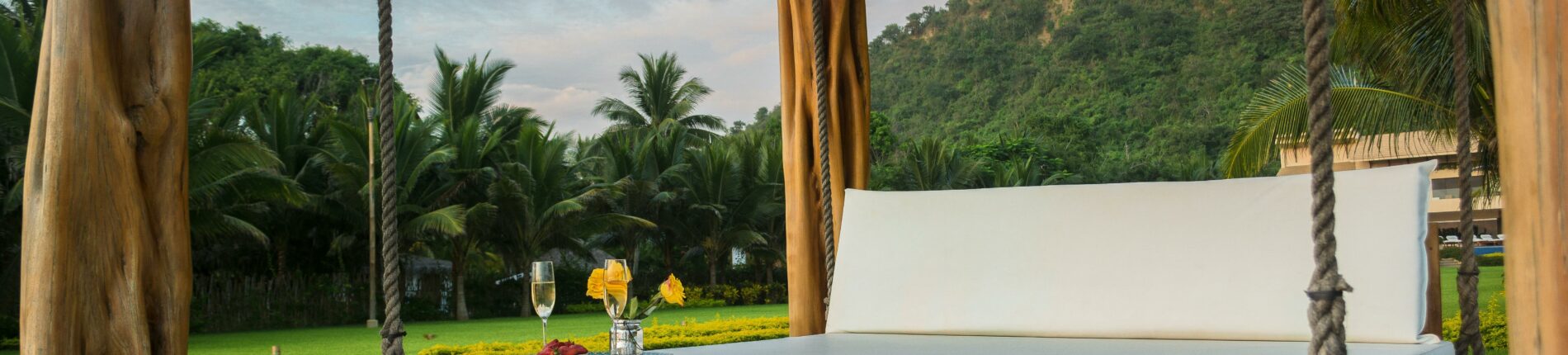 A luxurious swing bed under a wooden canopy with tropical palm trees.