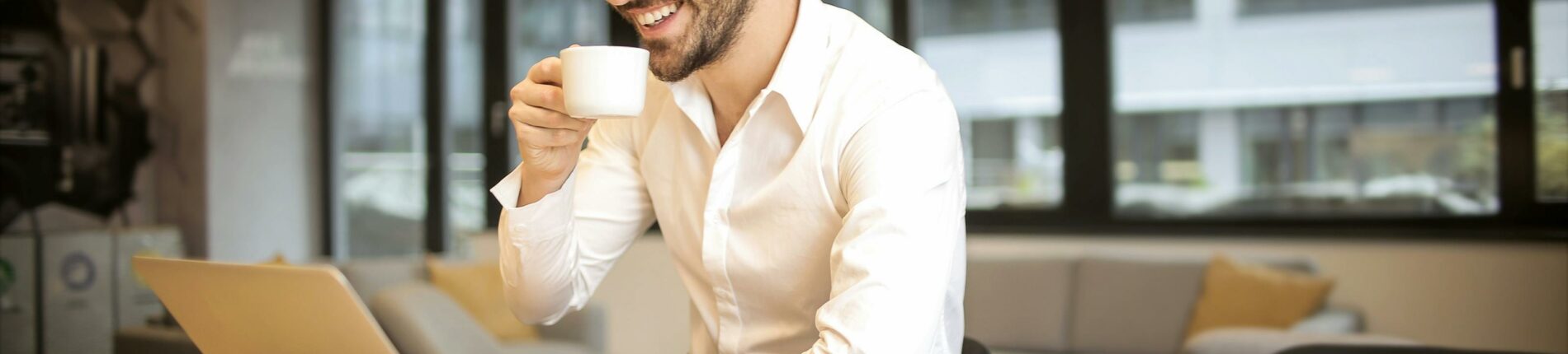 Man enjoying a coffee break while working in a modern office with laptop and books.