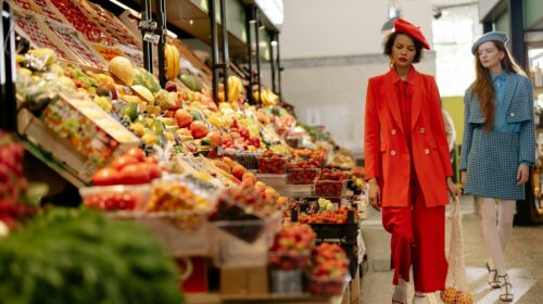 Fashionable women in vibrant outfits shopping for fresh produce in a lively supermarket.
